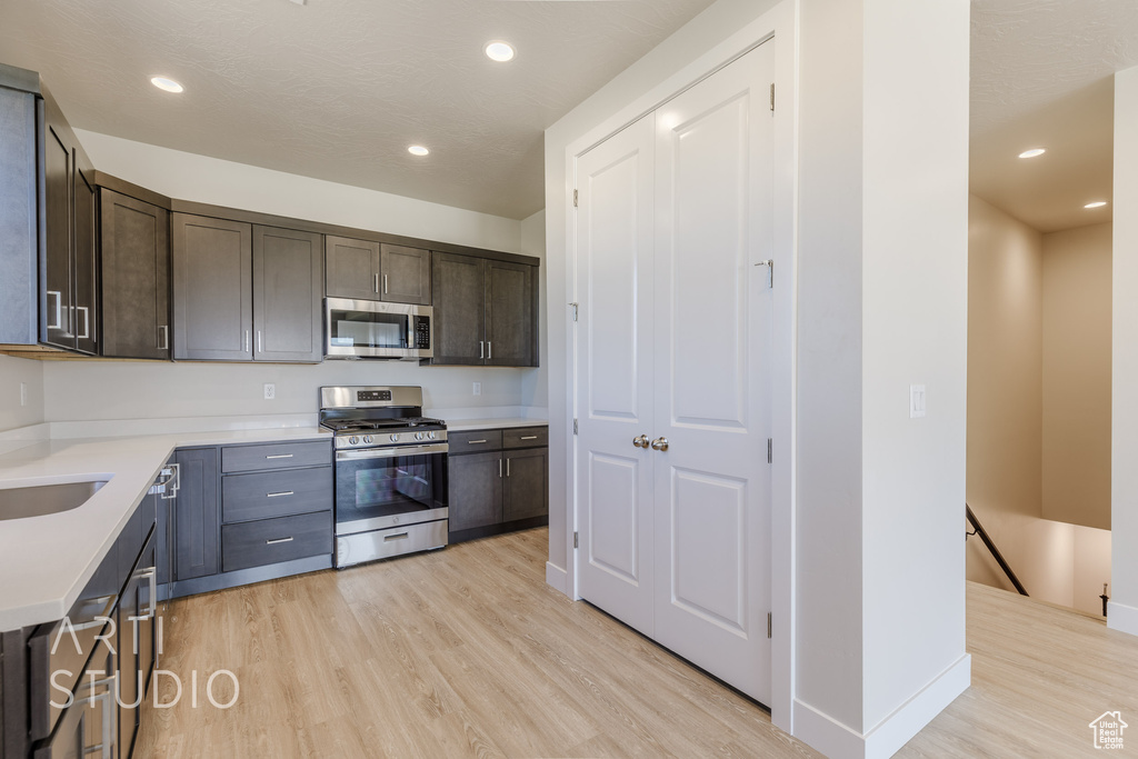 Kitchen with dark brown cabinets, appliances with stainless steel finishes, and light wood-type flooring