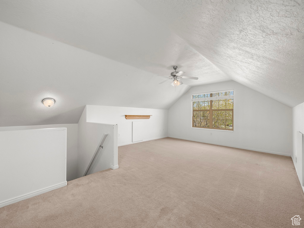 Additional living space featuring light carpet, lofted ceiling, ceiling fan, and a textured ceiling