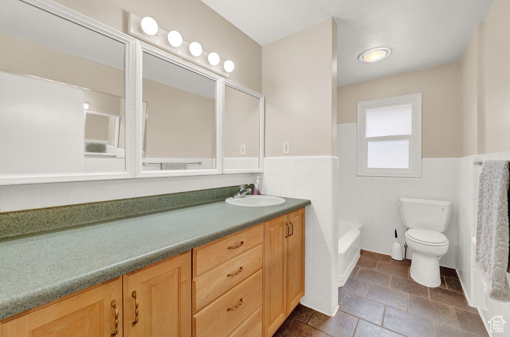 Bathroom featuring tile floors, tile walls, toilet, and vanity with extensive cabinet space
