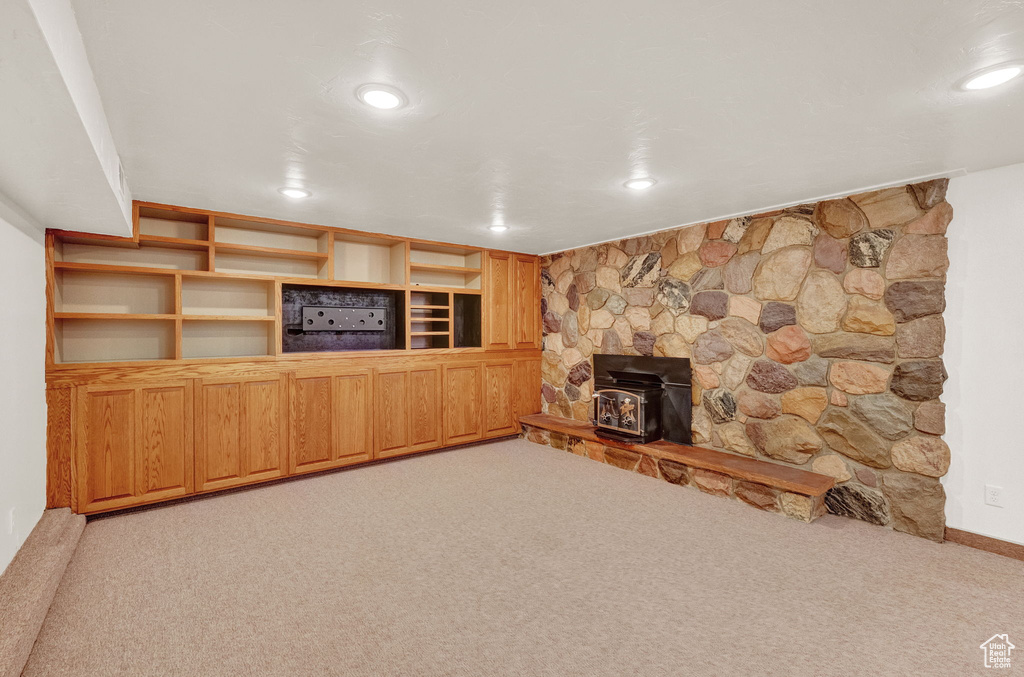 Unfurnished living room with light carpet, a stone fireplace, and a wood stove
