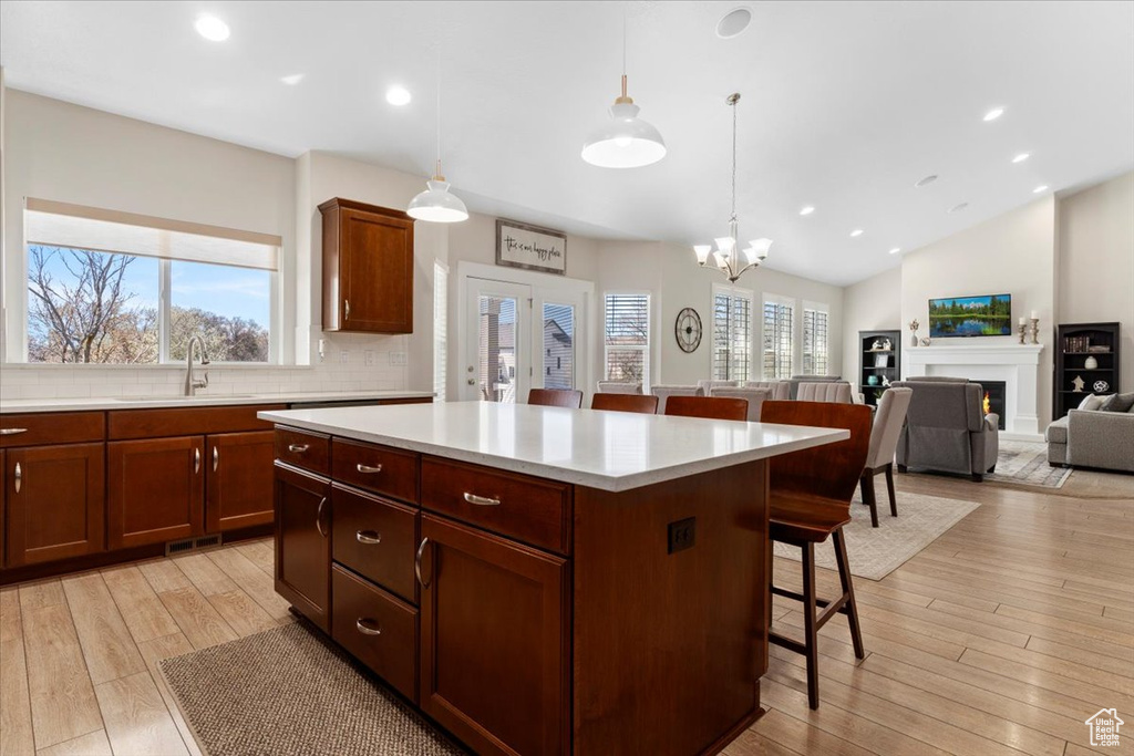 Kitchen featuring a kitchen island, backsplash, a breakfast bar area, hanging light fixtures, and light hardwood / wood-style flooring