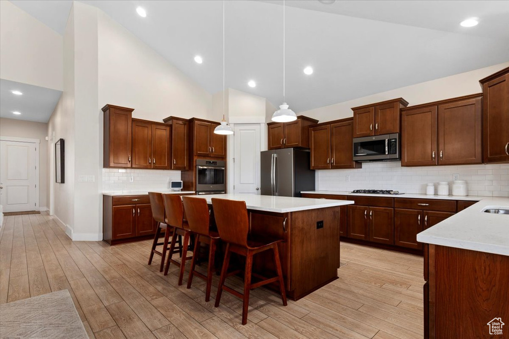 Kitchen featuring a center island, hanging light fixtures, light hardwood / wood-style flooring, backsplash, and stainless steel appliances