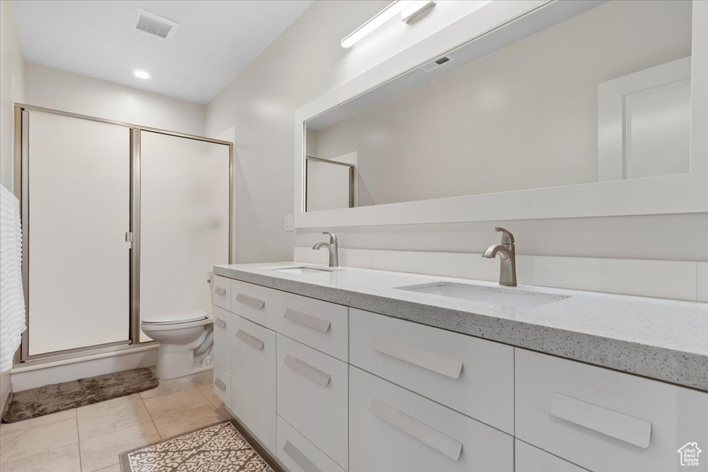 Bathroom featuring a shower with shower door, toilet, vanity with extensive cabinet space, double sink, and tile floors