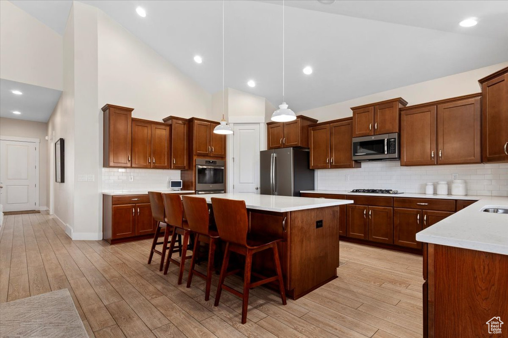 Kitchen with a kitchen island, light hardwood / wood-style flooring, backsplash, stainless steel appliances, and hanging light fixtures