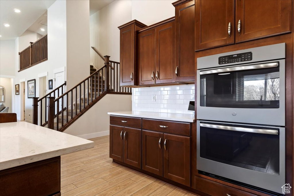 Kitchen with light hardwood / wood-style floors, tasteful backsplash, double oven, and light stone countertops