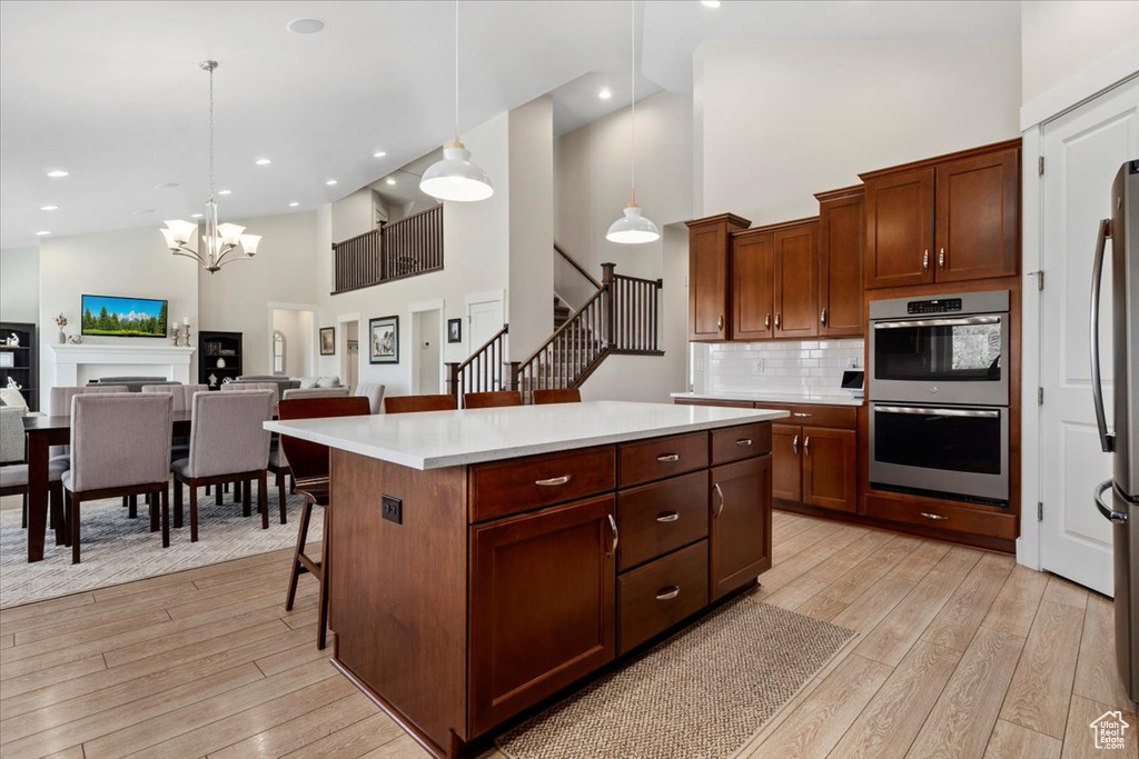 Kitchen with backsplash, decorative light fixtures, high vaulted ceiling, and light wood-type flooring