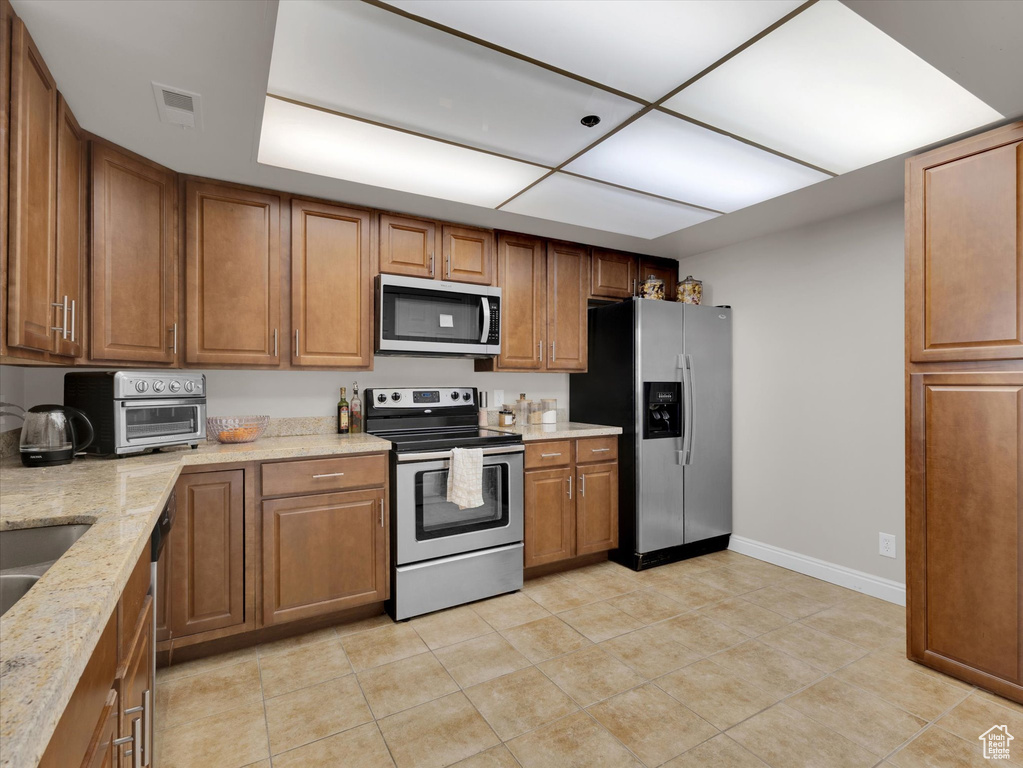 Kitchen with stainless steel appliances, light tile floors, and light stone counters