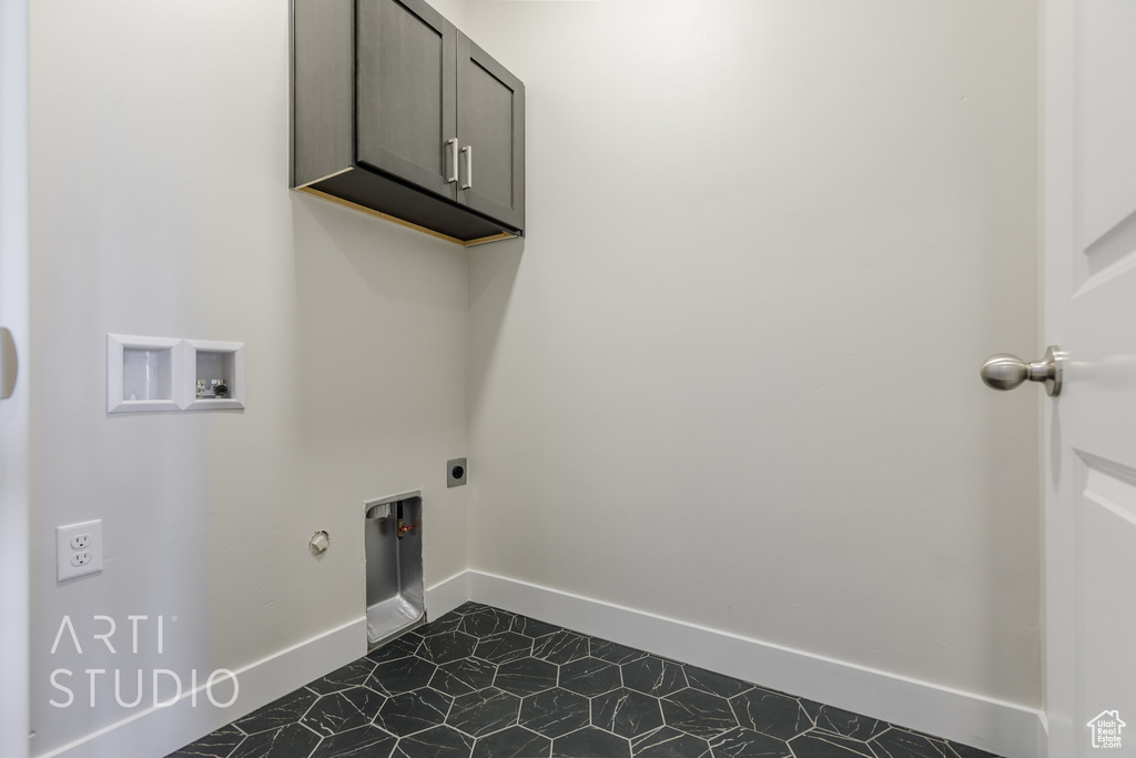 Laundry area with dark tile patterned flooring, hookup for a gas dryer, electric dryer hookup, washer hookup, and cabinets