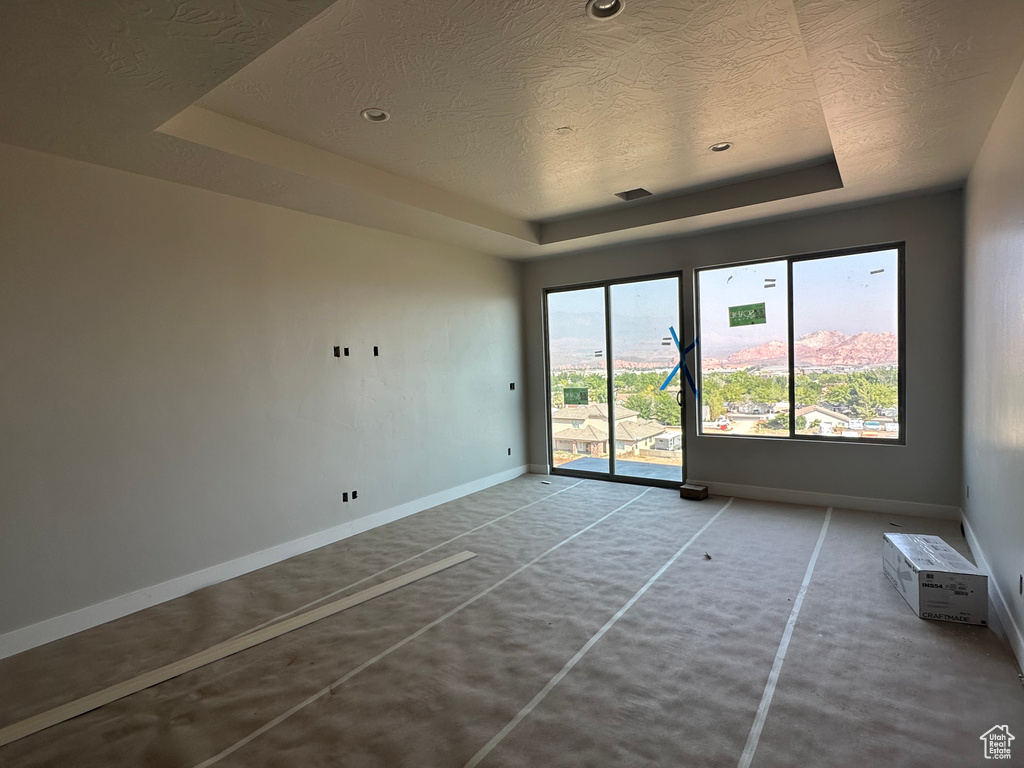 Empty room featuring a raised ceiling, a textured ceiling, and concrete floors