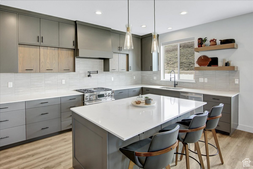 Kitchen featuring gray cabinets, premium range hood, appliances with stainless steel finishes, and a breakfast bar area