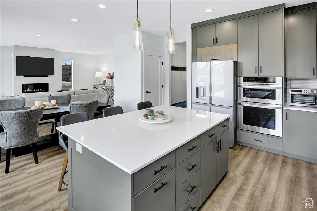 Kitchen with stainless steel double oven, a kitchen island, light hardwood / wood-style floors, and a kitchen breakfast bar