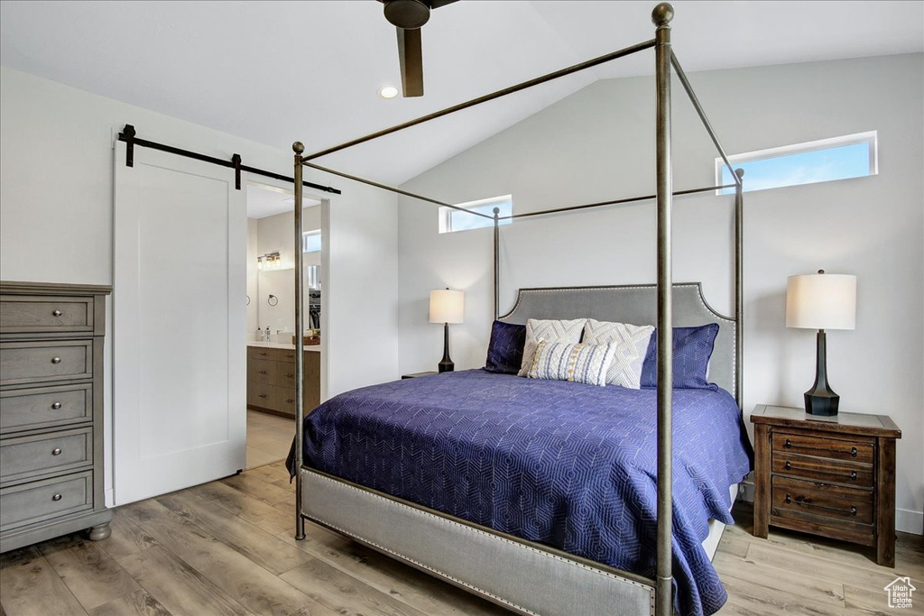 Bedroom with a barn door, ensuite bath, ceiling fan, light hardwood / wood-style floors, and lofted ceiling