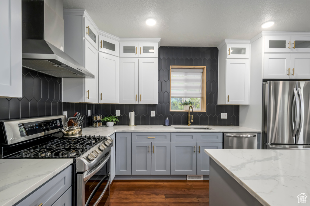 Kitchen featuring wall chimney exhaust hood, backsplash, appliances with stainless steel finishes, and sink