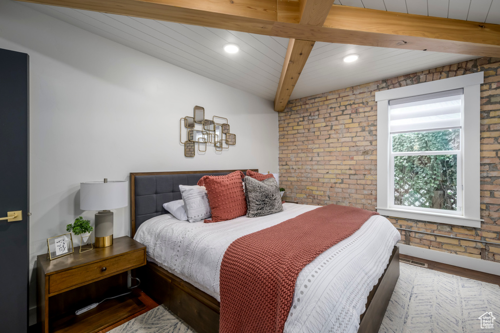 Bedroom with beamed ceiling, brick wall, and hardwood / wood-style flooring