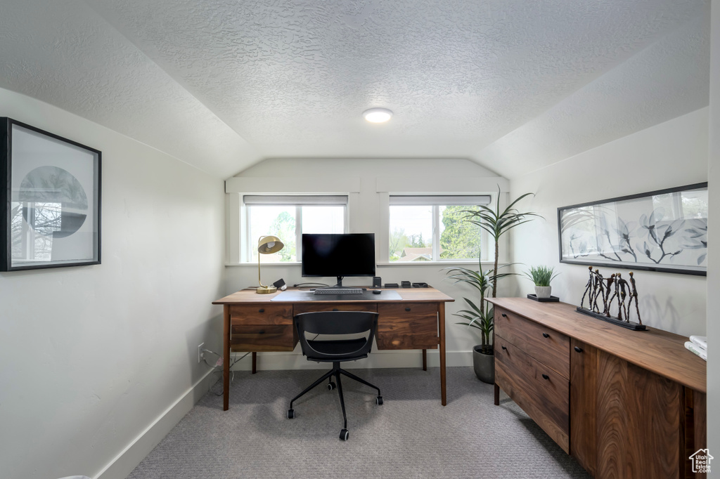 Carpeted office featuring vaulted ceiling and a textured ceiling