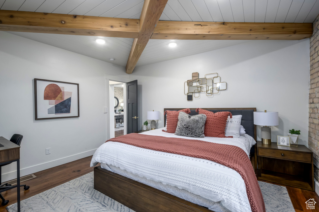 Bedroom featuring brick wall, dark hardwood / wood-style flooring, and beam ceiling