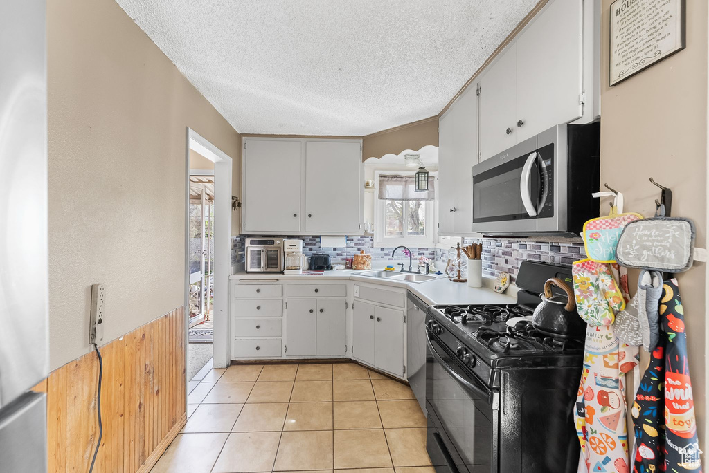 Kitchen featuring dishwashing machine, light tile flooring, tasteful backsplash, sink, and black gas range oven