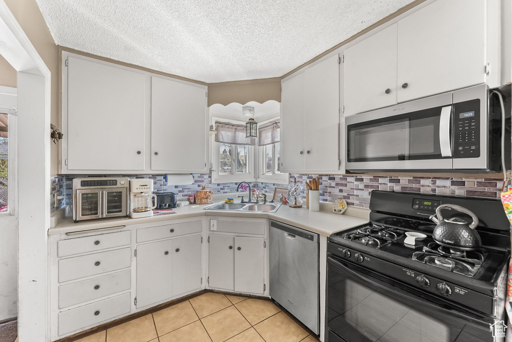 Kitchen with white cabinets, backsplash, stainless steel appliances, sink, and light tile floors