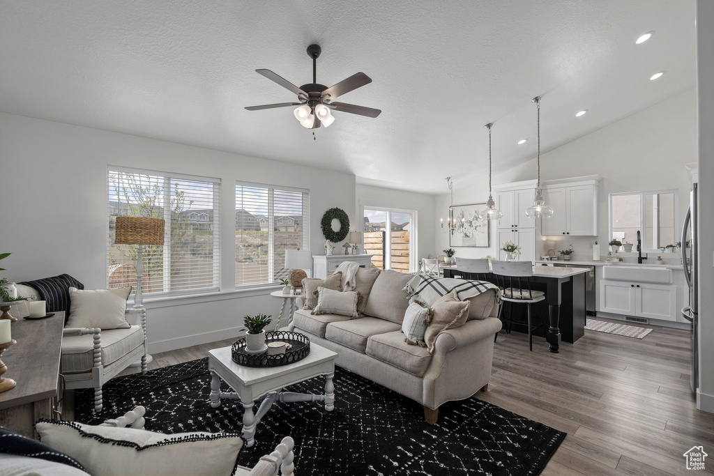 Living room featuring ceiling fan with notable chandelier, high vaulted ceiling, and hardwood / wood-style floors