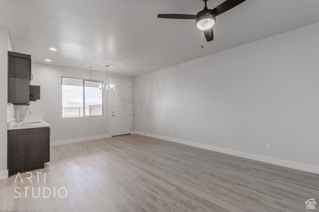 Unfurnished living room featuring sink, light hardwood / wood-style flooring, and ceiling fan with notable chandelier