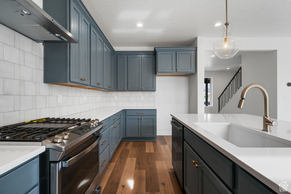 Kitchen featuring stainless steel gas range, wall chimney exhaust hood, sink, tasteful backsplash, and dark wood-type flooring