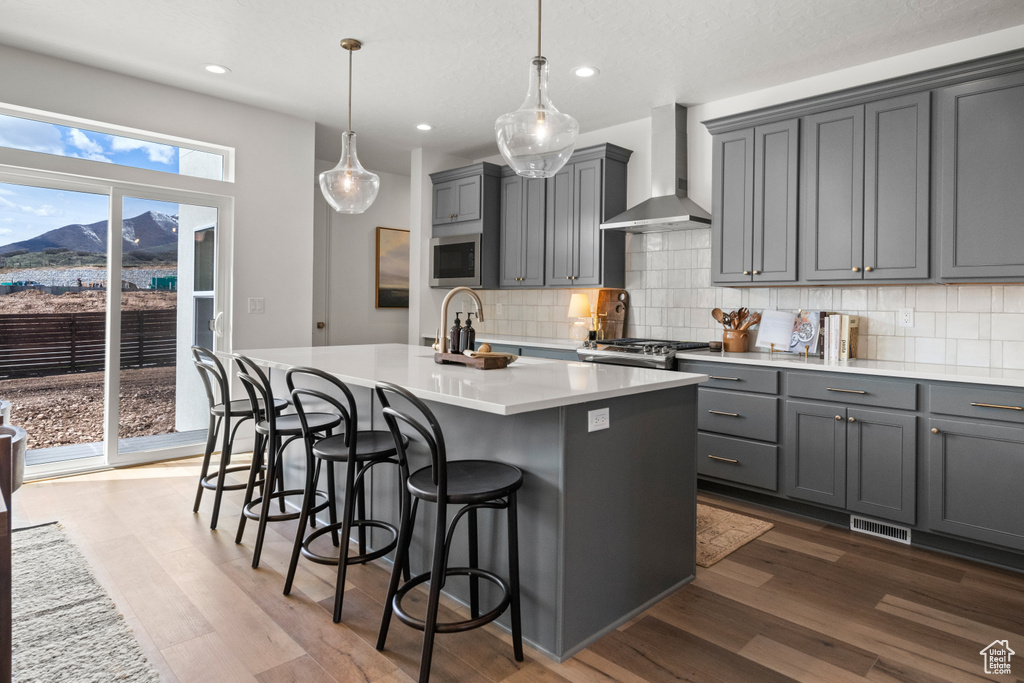 Kitchen featuring backsplash, wall chimney range hood, a kitchen island with sink, and dark hardwood / wood-style flooring