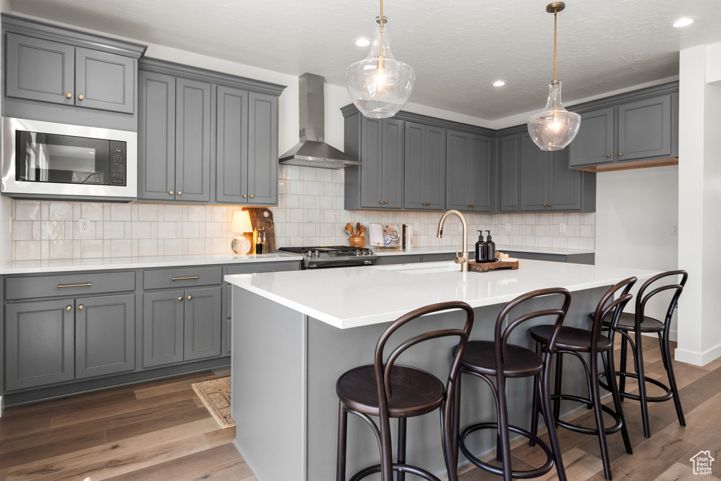 Kitchen featuring tasteful backsplash, wall chimney range hood, dark wood-type flooring, and sink