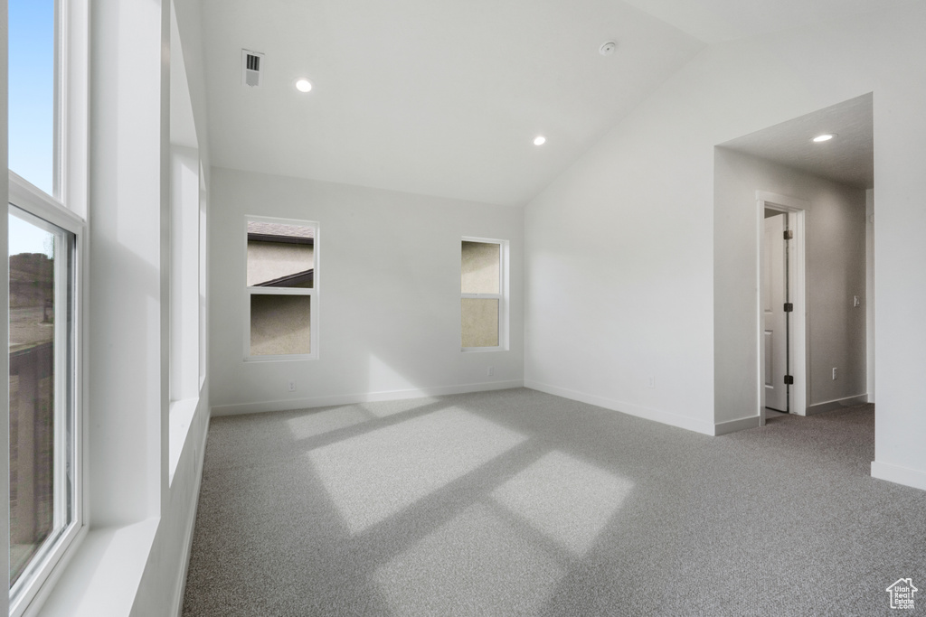 Carpeted spare room featuring plenty of natural light and vaulted ceiling