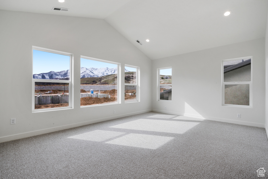 Empty room with a mountain view, light colored carpet, and high vaulted ceiling