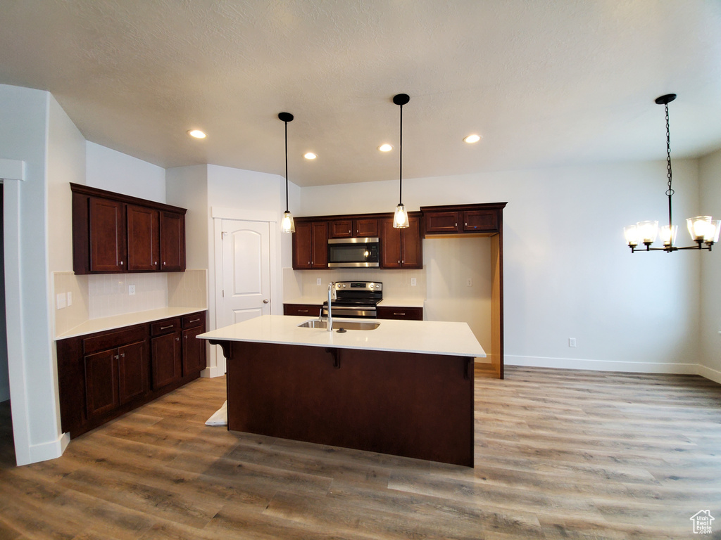 Kitchen featuring appliances with stainless steel finishes, pendant lighting, a notable chandelier, hardwood / wood-style floors, and a kitchen island with sink