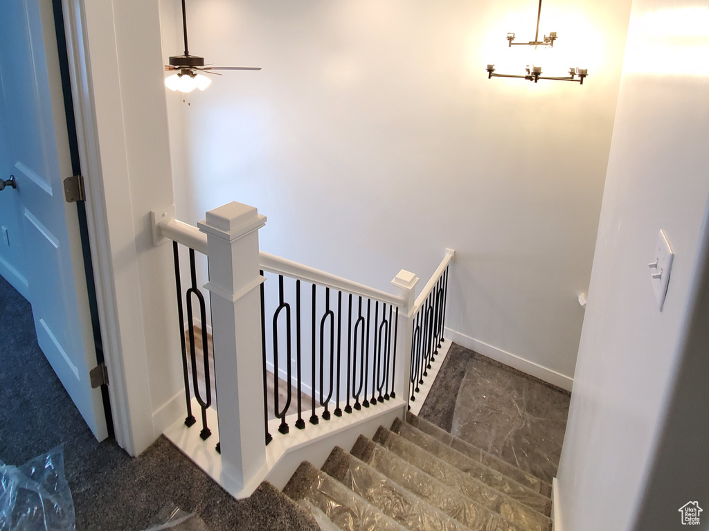 Stairway with dark tile floors and ceiling fan with notable chandelier