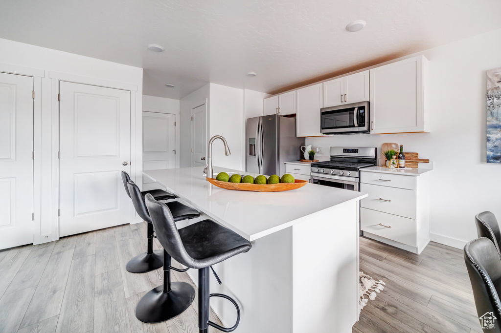 Kitchen featuring appliances with stainless steel finishes, light hardwood / wood-style flooring, an island with sink, white cabinetry, and a kitchen breakfast bar