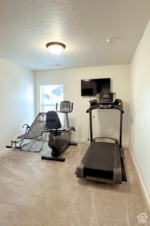 Exercise area with light colored carpet and a textured ceiling