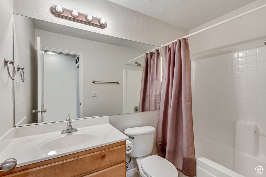 Full bathroom featuring a textured ceiling, oversized vanity, toilet, and shower / bathtub combination with curtain