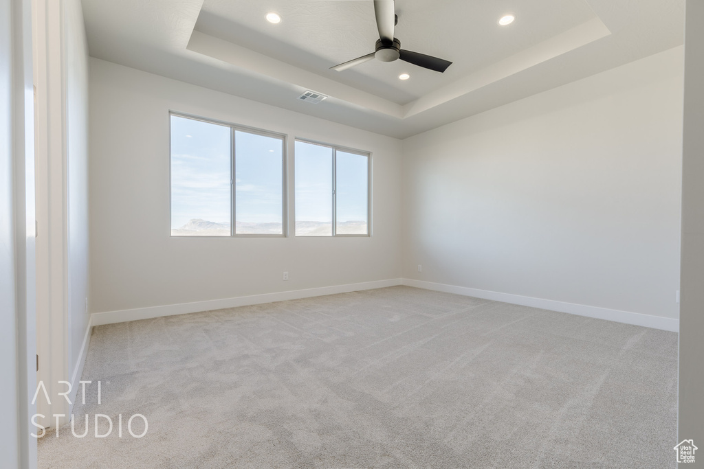 Carpeted empty room featuring ceiling fan and a raised ceiling