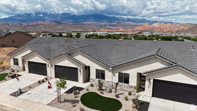 Ranch-style house with concrete driveway, stucco siding, a mountain view, a garage, and stone siding
