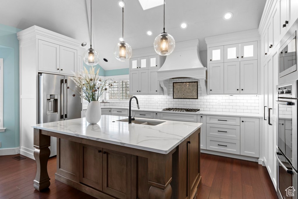 Kitchen featuring light stone countertops, a center island with sink, dark hardwood / wood-style floors, tasteful backsplash, and custom exhaust hood