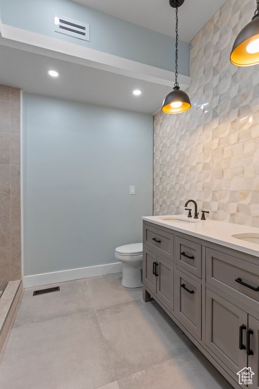 Bathroom featuring tile walls, backsplash, toilet, tile floors, and dual bowl vanity