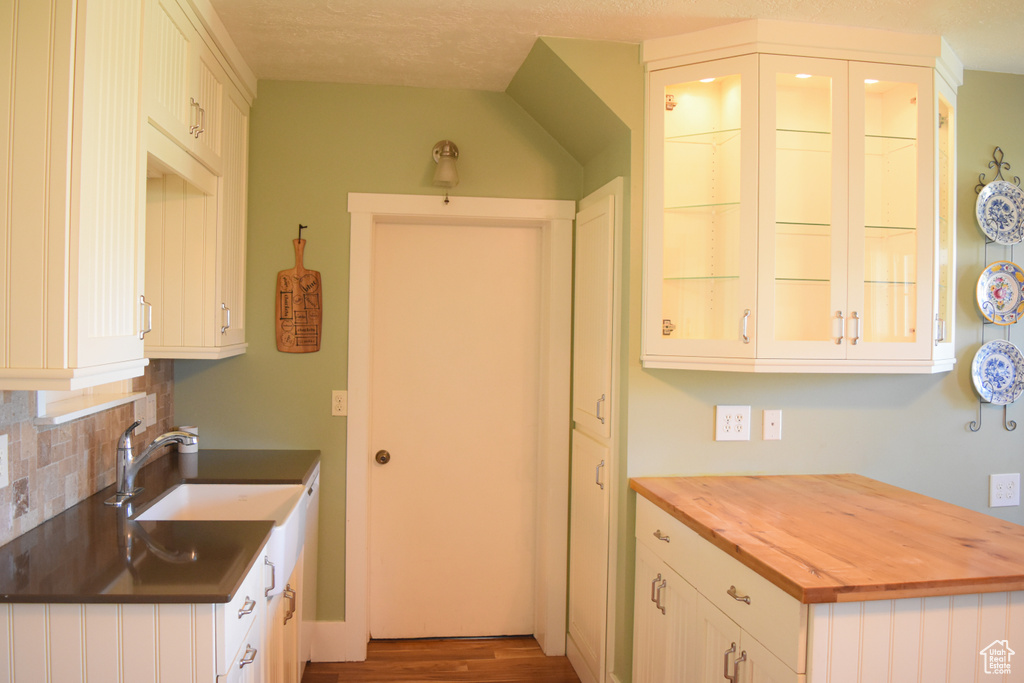 Kitchen with white cabinets, sink, backsplash, dark wood-type flooring, and butcher block counters