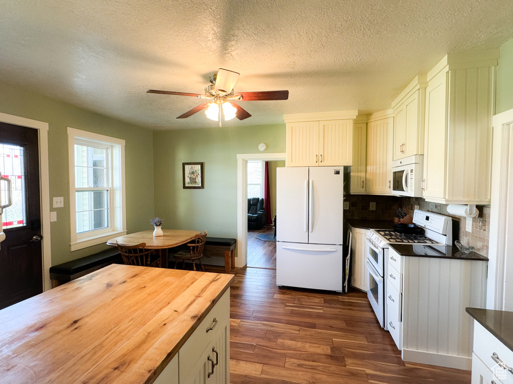 Kitchen with a healthy amount of sunlight, tasteful backsplash, dark wood-type flooring, and white appliances
