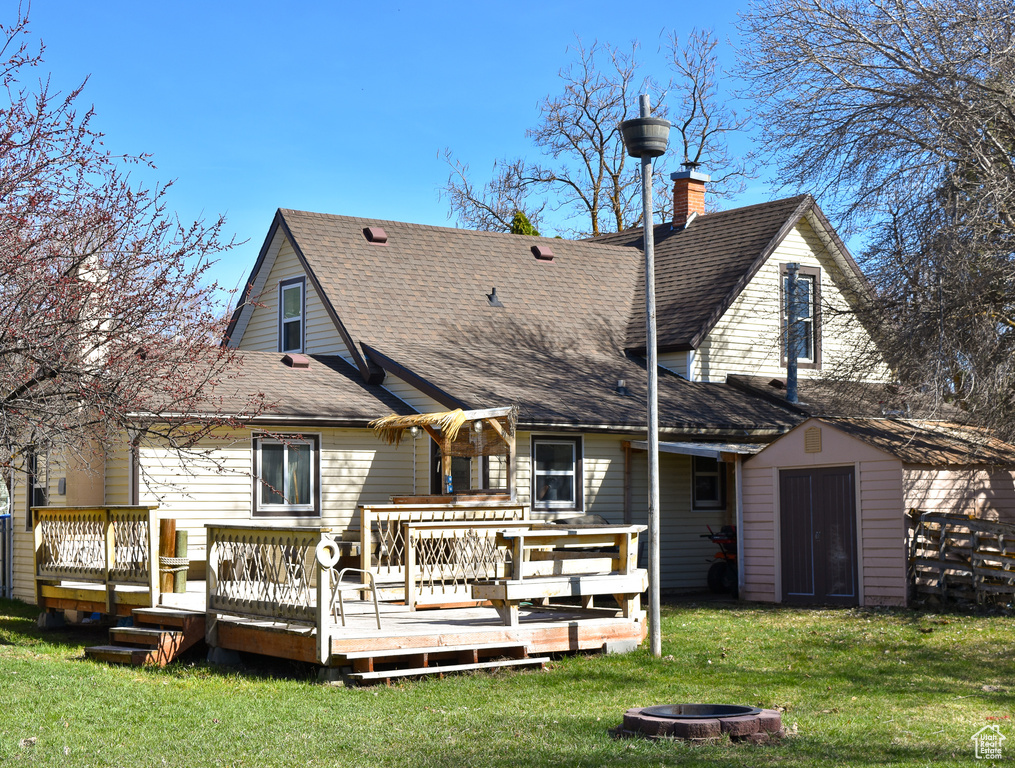 Back of house with a fire pit, a wooden deck, and a lawn