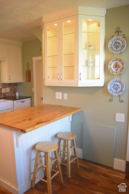 Kitchen featuring dark hardwood / wood-style flooring, wood counters, a kitchen breakfast bar, and white dishwasher