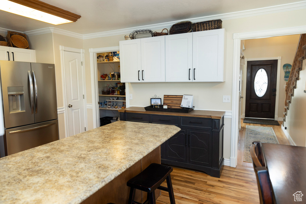 Kitchen featuring white cabinets, light wood-type flooring, ornamental molding, a kitchen bar, and stainless steel fridge
