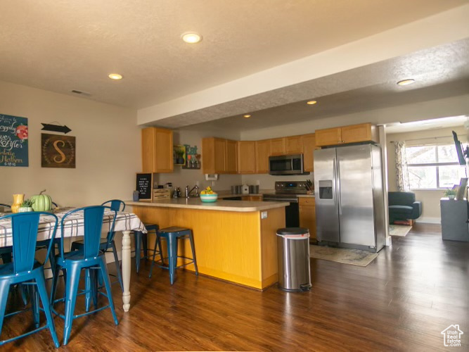 Kitchen with a breakfast bar area, kitchen peninsula, stainless steel appliances, and dark hardwood / wood-style floors