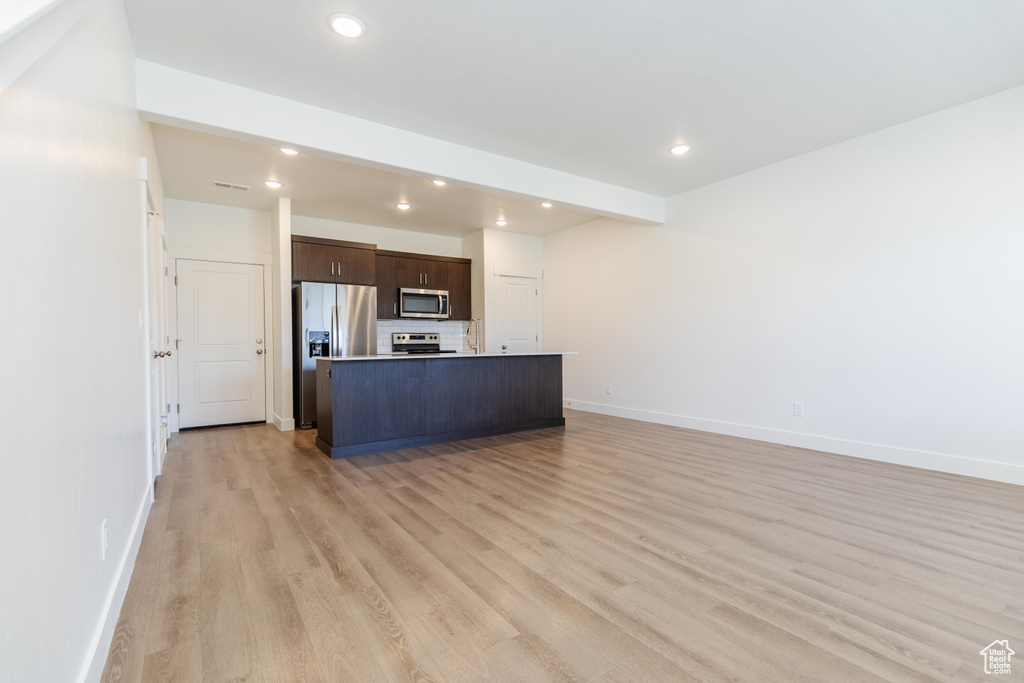 Kitchen with light hardwood / wood-style floors, tasteful backsplash, dark brown cabinets, stainless steel appliances, and a kitchen island with sink