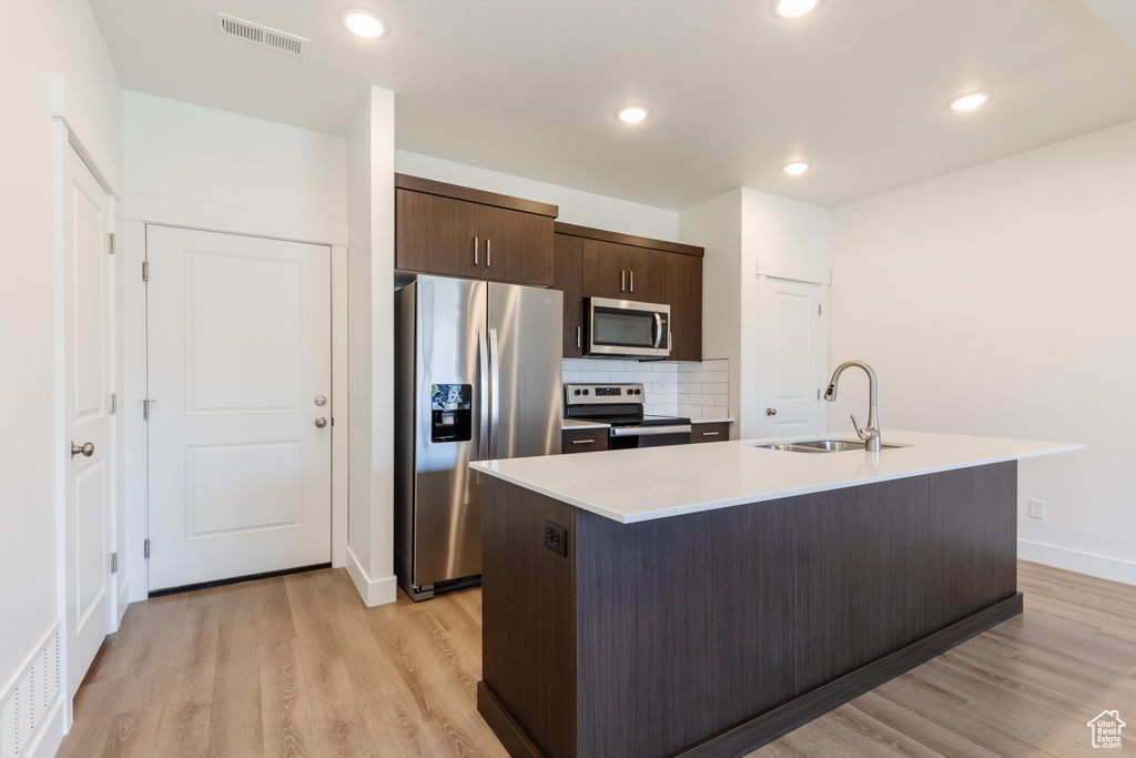 Kitchen featuring appliances with stainless steel finishes, sink, light hardwood / wood-style floors, and a kitchen island with sink