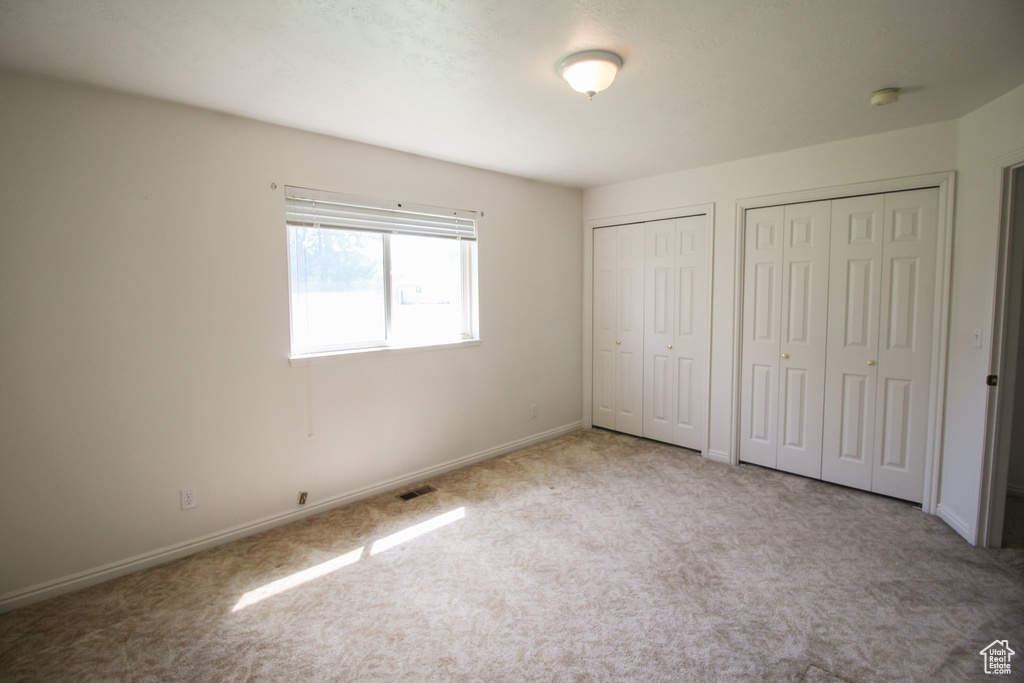 Unfurnished bedroom featuring light colored carpet and multiple closets