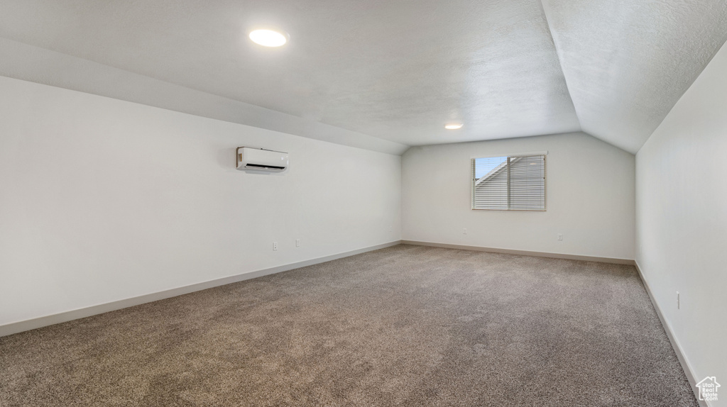 Carpeted empty room featuring vaulted ceiling and an AC wall unit