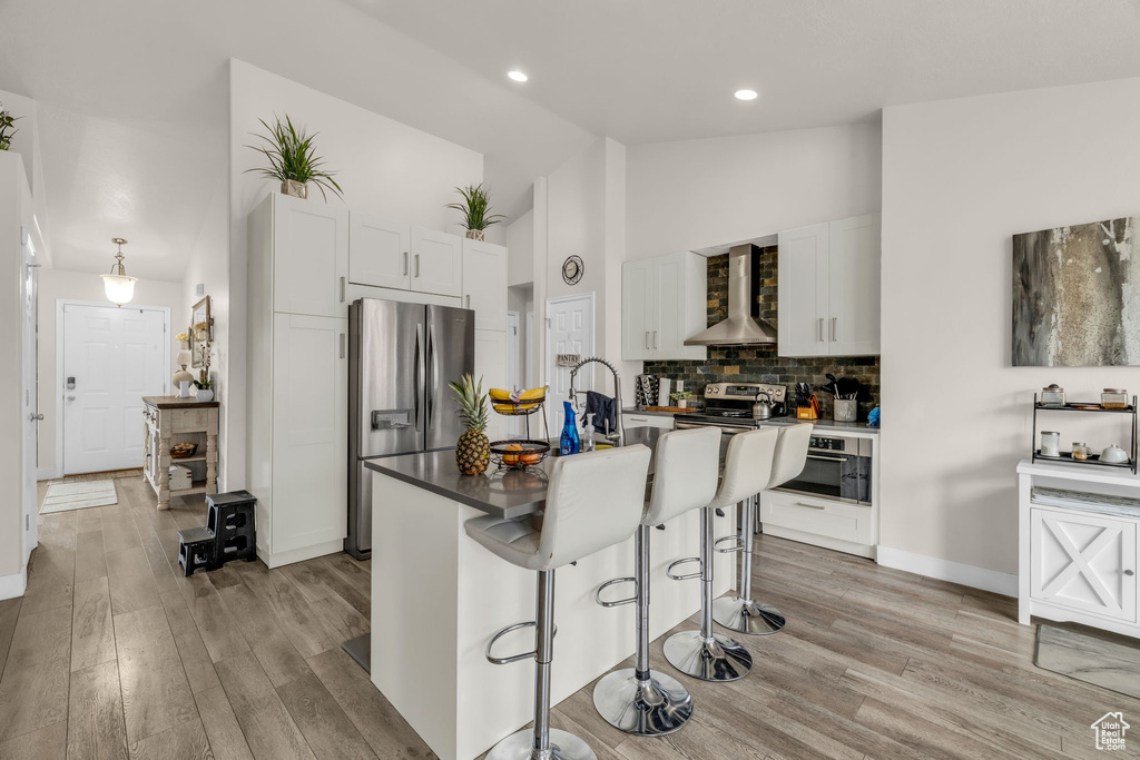 Kitchen with white cabinets, light hardwood / wood-style floors, appliances with stainless steel finishes, and wall chimney exhaust hood