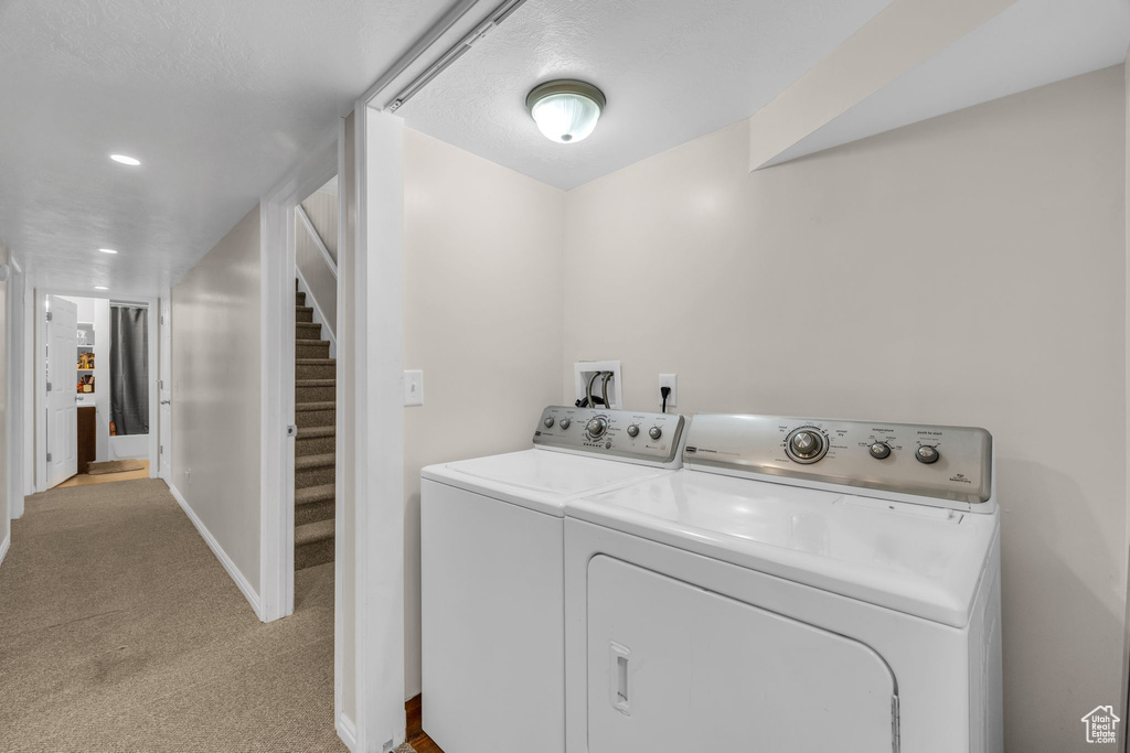 Clothes washing area with light colored carpet, washer and dryer, hookup for a washing machine, and a textured ceiling
